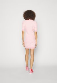 Abito rosa lavorato a maglia con maniche corte, design aderente e orlo a costine, abbinato a sneakers rosa con accenti floreali.