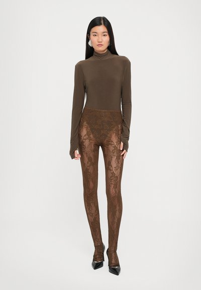 Brun langermet topp i kombinasjon med semitransparent brune blomstermønstrete lace leggings. Tettsittende design med intrikate bladmønstre og konturering. Sorte hælesko.