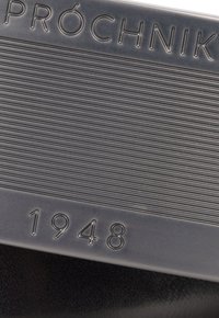 Czarna teksturowana powierzchnia z pionowymi liniami; wytłoczone "PROCHNIK" u góry i "1948" na dole, wskazujące markę i rok założenia.