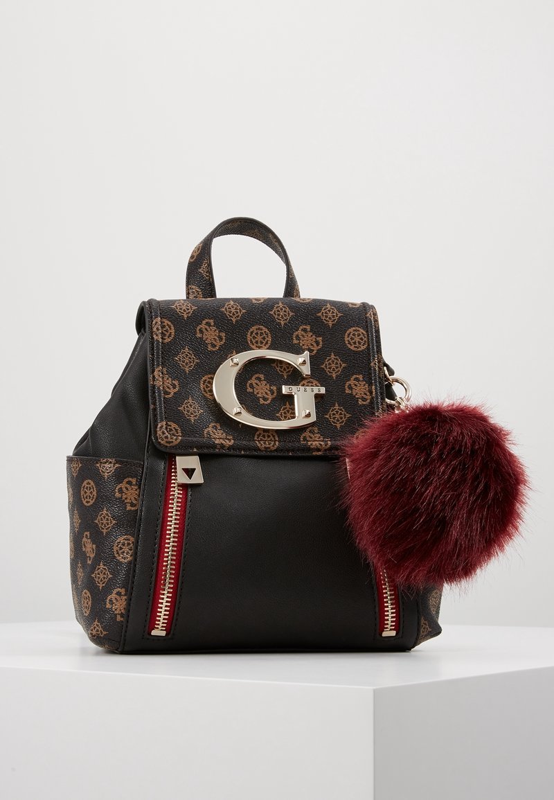 Sac à dos à motifs noirs et bruns avec un pompon en fausse fourrure bordeaux, ferrures dorées et accents de fermeture éclair rouges. Conception structurée avec poignée supérieure.