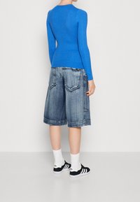 Niebieski sweter z długim rękawem w prążki, połączony z szortami z jasnoniebieskiego denimu do kolan oraz czarnymi sneakersami w białe paski, stylizowany z białymi skarpetami.