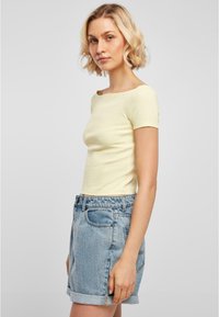Ljusgul figursydd t-shirt med korta ärmar, fyrkantig halsringning, kombinerad med högmidjade, ljusblå denimshorts med uppvikta kanter.