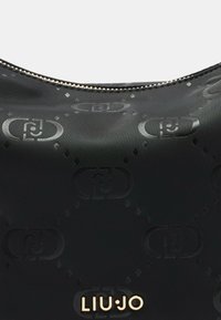 Borsa nera in nylon con un delicato motivo a logo stampato, chiusura con zip e un'emblema metallico del marchio. Texture liscia con dettagli raffinati.