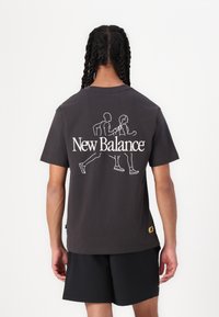 Dark gray cotton t-shirt featuring a white outline graphic of two runners and "New Balance" in bold lettering on the back. Short sleeves.
