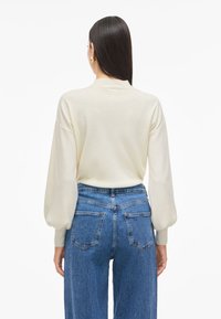 Cream sweater with a round neck and puffed sleeves, paired with high-waisted blue denim jeans featuring back pockets and a relaxed fit.