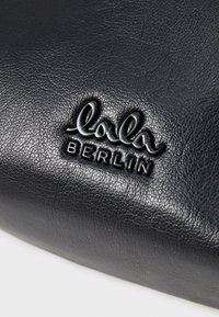 Mustan nahkaiseen asusteeseen on painettu "lala BERLIN" -logo. Pinnassa on teksturoitu viimeistely.