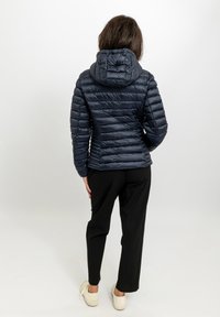 Giacca imbottita blu navy con design aderente, cuciture orizzontali a rilievo e cappuccio staccabile, abbinata a pantaloni neri e sneaker bianche.