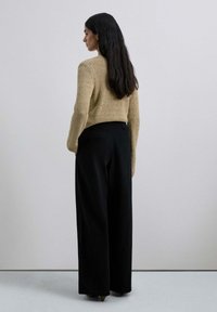 Suéter de punto beige con patrón texturizado, combinado con pantalones de pierna ancha negros de cintura alta. Modelo de espaldas, con el cabello largo y oscuro.