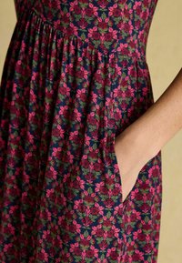 Kleid aus floral gemustertem Stoff mit pinken und grünen Blumen auf einem dunkelblauen Hintergrund, mit geraffter Taille und seitlichen Taschen.