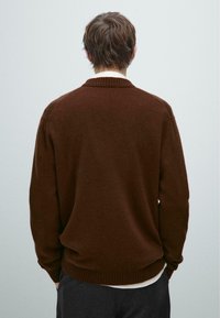 Brauner Strickpullover mit geripptem Kragen und Bündchen, in lässiger Passform und weicher Textur, von hinten vor einem hellen Hintergrund präsentiert.