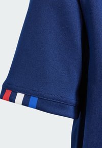 Krátky rukáv modrá polo košeľa s textúrovanou tkaninou. Obsahuje červené, biele a modré pruhy na okraji manžety.