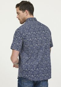 Chemise à manches courtes en tissu bleu marine, avec un motif floral blanc. Coupe décontractée avec col et ourlet droit, confectionnée dans un matériau léger.