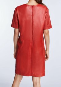 Robe en cuir rouge avec des manches courtes, un col rond et une fermeture éclair au dos. Texture lisse, longueur genou et silhouette ajustée.