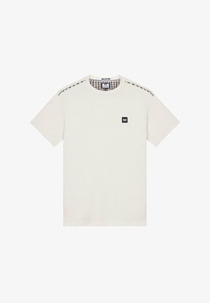 Krémové tričko s kulatým výstřihem, kontrastní kostkovaná látka na ramenou a malá černá logo na hrudi.