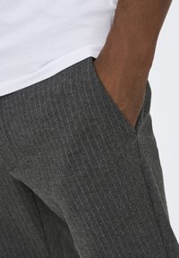 Pantalones de raya diplomática grises con una textura suave, que cuentan con un bolsillo lateral y una silueta ajustada. Complementados con una camiseta blanca en la parte superior.