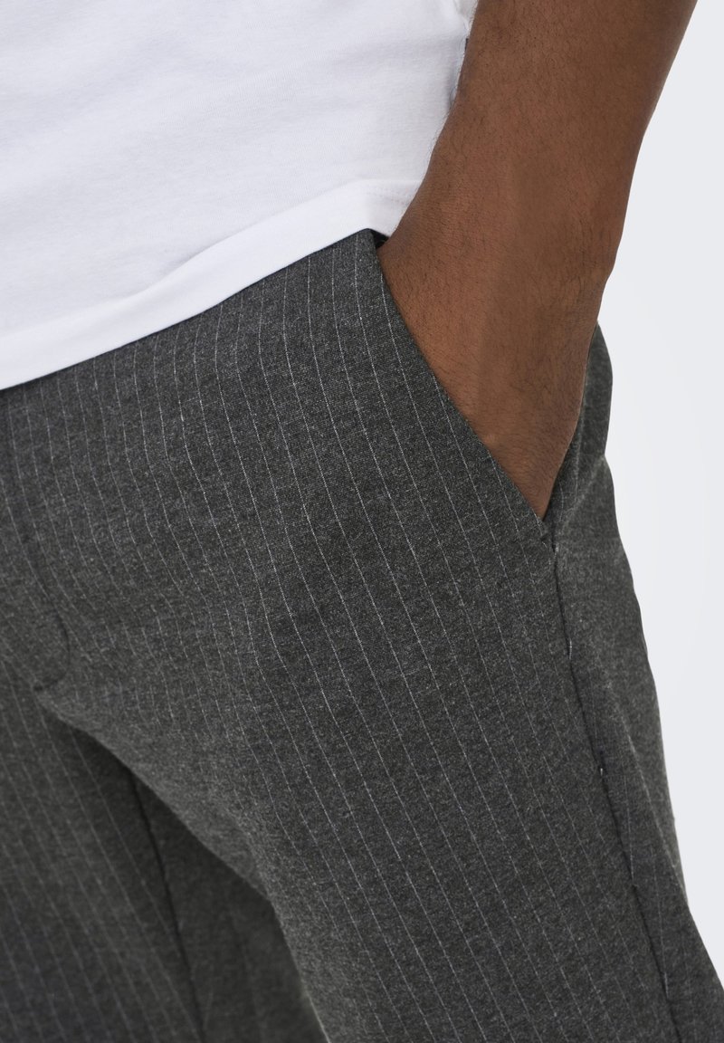 Pantaloni grigi a righe sottili con una texture morbida, dotati di tasca laterale e silhouette aderente. Abbinati a una t-shirt bianca sulla parte superiore.