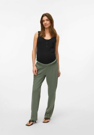 Black sleeveless top with button placket and green, loose-fitting pants with a gathered waistband, worn with flat sandals.