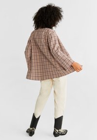 Gepäckte übergroße Jacke in Beige- und Brauntönen mit weiten Ärmeln und abgerundetem Saum, kombiniert mit cremefarbenen Hosen und schwarzen Stiefeln.