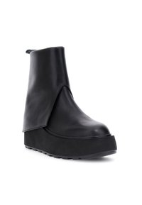 Stivale alla caviglia in pelle nera con un design minimalista, suola a piattaforma nascosta e una patta asimmetrica sulla parte anteriore.