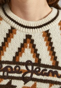 Primo piano di un maglione lavorato a maglia con motivi geometrici marroni e arancioni e ricami cursivi marrone scuro sul petto.