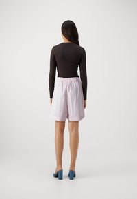 Svart langermet topp kombinert med lyserosa shorts med elastisk midje. Antrekket er fullført med blå blokkhæl sandaler.