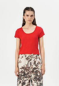Haut rouge à manches courtes avec un décolleté arrondi, fabriqué à partir d'un tissu doux. Associé à un pantalon beige présentant un motif de taches brunes irrégulières.