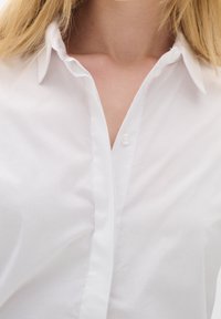Biała koszula z guzikami, posiadająca klasyczny kołnierzyk, długie rękawy oraz gładki, lekki materiał z delikatnym połyskiem.