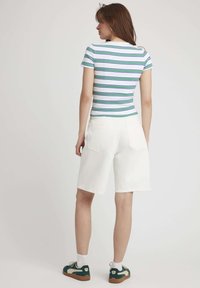 Shorts en denim blanc avec deux poches arrières, accompagnés d'un haut ajusté à manches courtes à rayures bleues et vertes sur fond blanc.