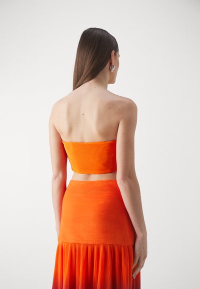 Oranža divdaļīga apģērba komplekts ar strapless topu un svārkiem ar krokām. Audumam ir teksturēta virsma un atšķirīgas oranžas nokrāsas.