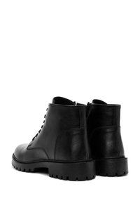 Botas de tobillo de cuero negro con un acabado texturizado, parte delantera con cordones y suela de goma gruesa con un patrón robusto.