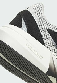 Athletisk sko med ovandel i mesh, huvudsakligen svart och silver, med texturerad yttersula och "LIGHTSTRIKE"-märkning på mellansulan.