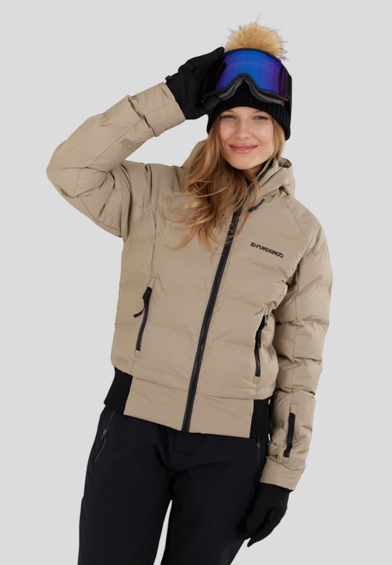 Beige pufferjack met een zwarte rits, zijzakken en geribbelde zoom. Gedeeltelijk gedragen met een zwarte hoed met een bontpompon en blauwe skibril.