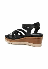 Sandalias de cuña negras de cuero con tiras entrecruzadas, una plantilla acolchada y una suela de plataforma en marrón claro. Detalles texturizados cerca del dedo del pie.