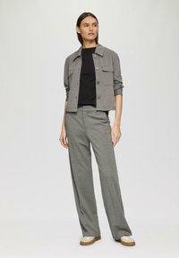 Veste grise à boutonnière avec poches plaquées, associée à un haut noir côtelé et à un pantalon large gris. Tissu texturé, coupe décontractée.