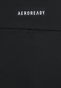 Leggings atléticos pretos feitos de um tecido liso e elástico. Apresentam uma cintura plana com "AEROREADY" em texto branco.