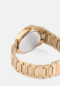 Relógio de pulso dourado com bracelete metálico e elos retangulares, apresentando uma caixa redonda e um fundo texturizado em prata. À prova de água até 50 metros.