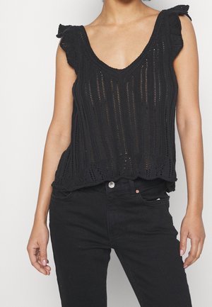 Zwarte gebreide tanktop met een V-hals, voorzien van ruches aan de mouwen, open geweven patroon en scalloped zoom, gecombineerd met zwarte jeans.