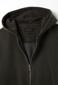 Giacca con cappuccio e zip in verde oliva scuro. Presenta un morbido rivestimento interno, una zip in metallo e un cappuccio regolabile. L'etichetta riporta la scritta "B ANGEL".