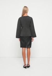 Top in misto lana grigia con maniche a campana, abbinato a una gonna a tubino in pelle nera. Sono visibili una superficie liscia e dettagli di design aderenti.