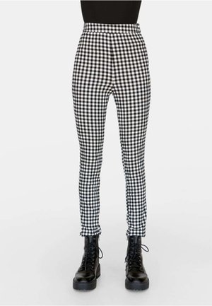 Schwarz-weiß karierte, schmal geschnittene Hose, kombiniert mit schwarzen Schnürstiefeln im Combat-Stil und einem schwarzen Oberteil, gezeigt von der Taille bis zu den Füßen.