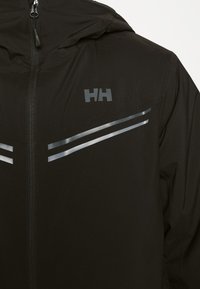 Schwarze, mit Reißverschluss versehenen Jacke aus glattem Stoff, ausgestattet mit reflektierenden silbernen Streifen und einem Logo für Sichtbarkeit und Stil. Inklusive Kapuze.