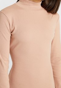 Haut à manches longues en tulle ajusté, fabriqué en tissu côtelé d'un doux rose poudré, avec un col montant et des détails de couture sans couture.