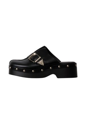 Sabot en cuir noir à enfiler avec boucle argentée et rivets métalliques ronds le long de la semelle épaisse, vue latérale en angle sur fond blanc.