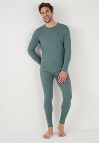 Men's thermal top and bottom set in muted teal, made of soft material, features long sleeves, fitted silhouette, and subtle logo detail.