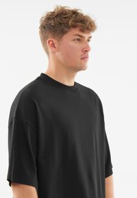 Tricou negru oversized cu guler rotund, mâneci scurte și un material fin, ușor. Prezintă o croială lejeră și un design minimalist.
