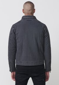 Szürke farmerdzseki strukturált gallérral, cipzáras ujjal és látható varrási részletekkel. Texturált anyag, laza szabással.