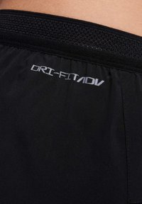 Shorts de sport noirs avec une ceinture élastique texturée, arborant un logo réfléchissant "DRI-FIT ADV" cousu sur le côté. Texture de tissu lisse.