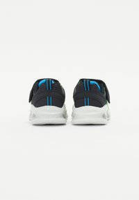 Scarpe da ginnastica nere con accenti verdi e blu, materiale in rete, cinturino in velcro e suole bianche imbottite. La vista posteriore mette in evidenza i dettagli delle cuciture.