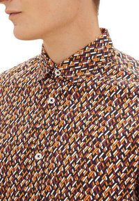 Shirt met een gestructureerde kraag, gemaakt van stof met een geometrisch patroon in oranje, wit en bordeaux op een donkere achtergrond.