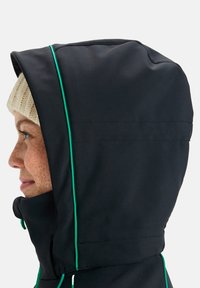 Veste à capuche noire avec des finitions vertes contrastantes, texture lisse et coupe près du visage avec un col haut pour plus de chaleur.